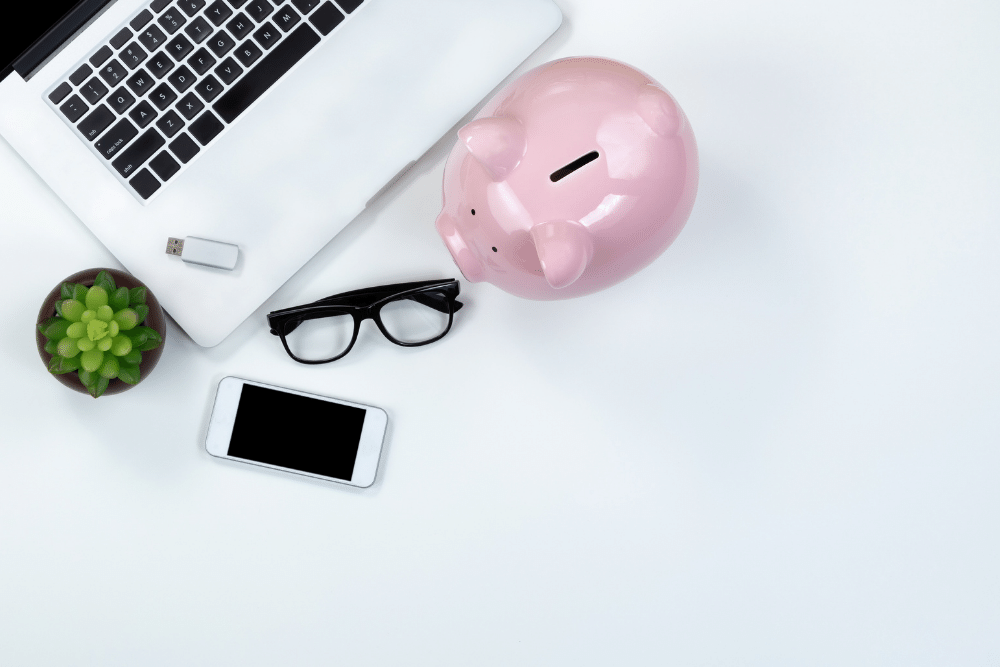 Piggie bank, glasses, phone and laptop on a white table