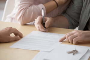 couple signing a contract with house keys by their hands