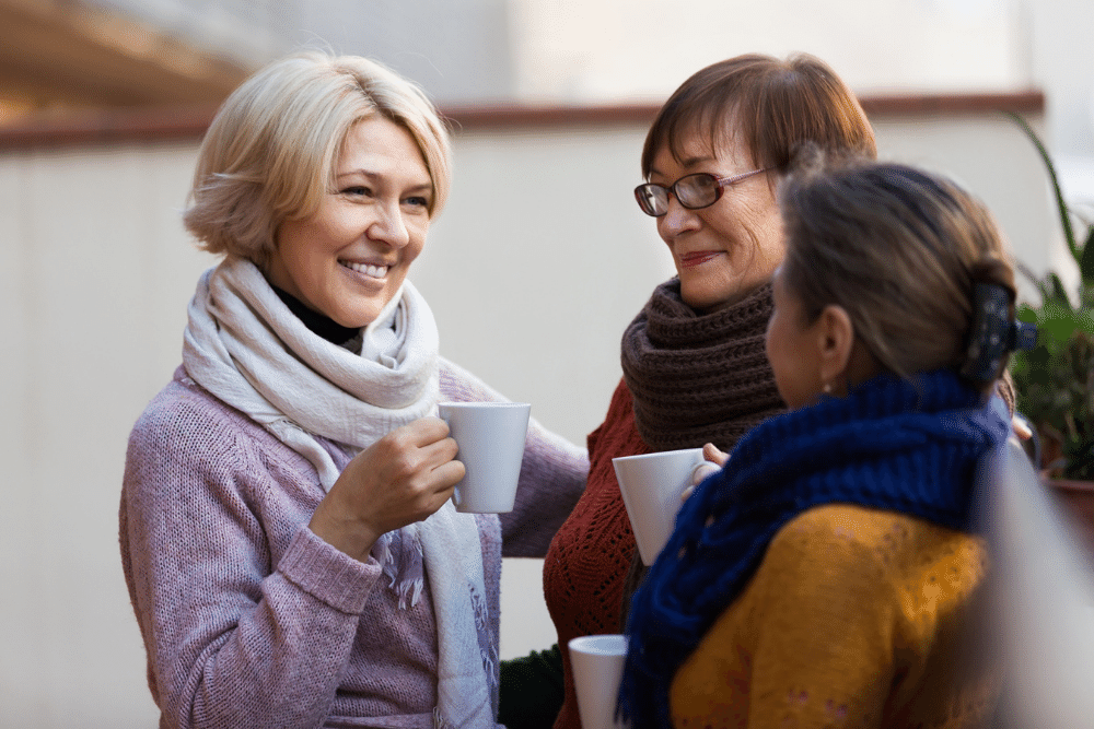 three women talking while holding white mugs
