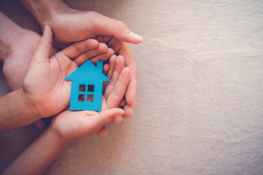 a child and adults hands holding a wooden house