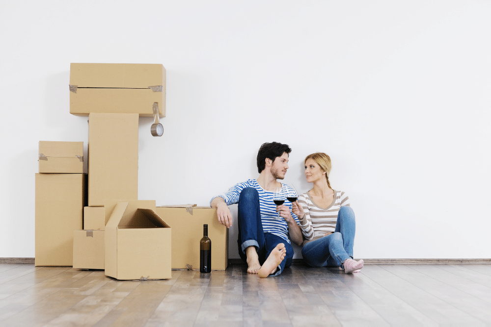 couple sat next to a pile of cardboard boxes on moving day