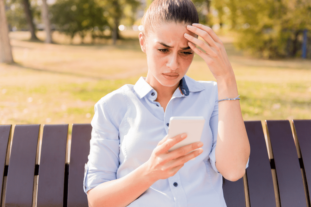 slightly distressed woman looking at her phone sat on a park bench