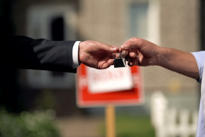 close up of hands as someone is given house keys with sold sign in background
